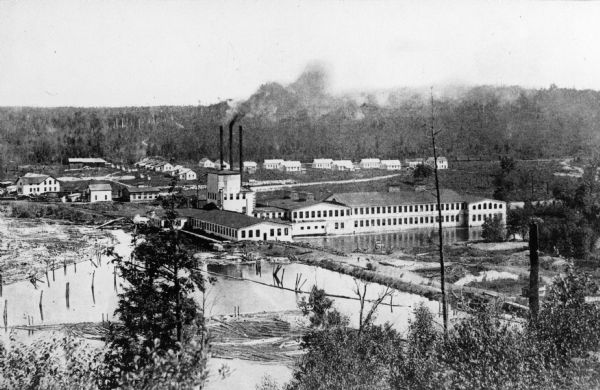 Elevated view of the Wausau paper mills, with smokestacks in the center, and trees and water in the foreground.