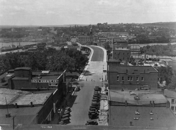 Elevated view of the main street with the Wisconsin River in the top left corner. The street just outside the Hall Garage Company is lined with cars.