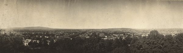 Panoramic elevated view over trees towards a residential area in Wausau, Wisconsin. Hills are in the distance.
