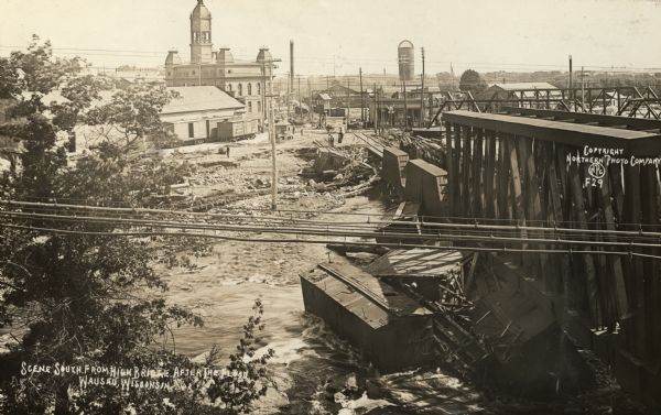 Elevated view across the Wisconsin River, showing the wreckage left by the disastrous flood of July 24, 1912. A power dam on the Wisconsin River above Wausau broke, releasing the waters of its reservoir on the city. (Scene is looking south from a bridge.) Caption reads: "Scene South from High Bridge After the Flood, Wausau, Wisconsin."