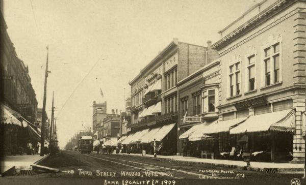 Winter view north up Third Street with businesses on both sides, and a trolley in the middle of the street further down the block. Caption reads: "Third Street Wausau, Wis. Same Locality in 1909".