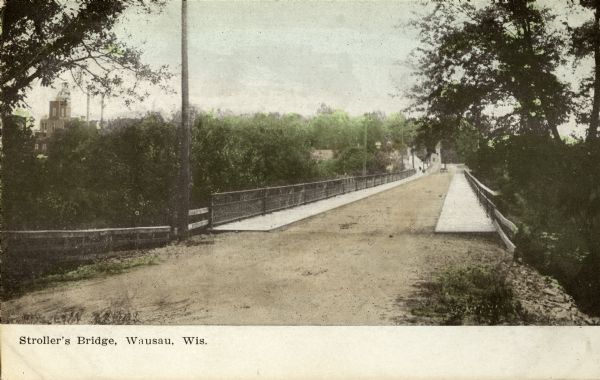 View down unpaved road towards Stroller's Bridge, with the city and a public building in the background. Caption reads: "Stroller's Bridge, Wausau, Wis."