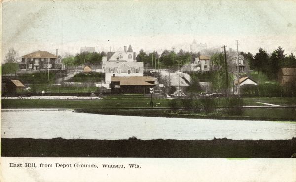 View across water toward East Hill. Caption reads: "East Hill, from Depot Grounds, Wausau, Wis."