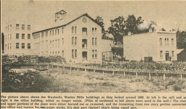 View of the Waukesha Woolen Mills buildings. Caption reads: "The picture above shows the Waukesha Woolen Mills buildings as they looked around 1880. At left is the mill and at right is the office building, which no longer exists. (Piles of cordwood at left above were used in the mill.) The rear and upper portions of the plant were either burned out or removed, and the remaining front two story portion converted late office and garage for the water works. It's that part (below) that's being razed now."