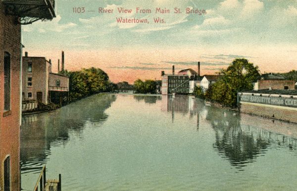 View from bridge with industrial buildings on both sides. Caption reads: "River view from Main St. Bridge, Watertown, Wis."
