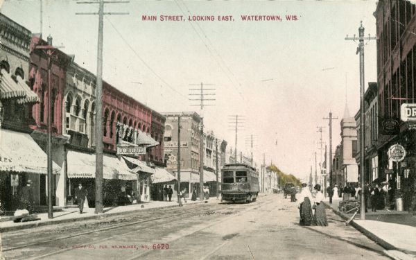 View across Main Street. A streetcar is coming up the street. Caption reads: "Main Street, Looking East, Watertown, Wis."