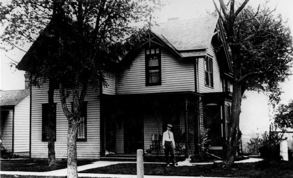 Exterior view of the Samuel E. Kuenzi home, located at 317 Dewey Avenue. A man and a dog are posing on the lawn in front.