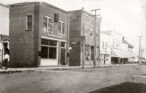 View of the buildings located on what is thought to be the east side of Main Street, including a physician and surgeon's office and a bank.