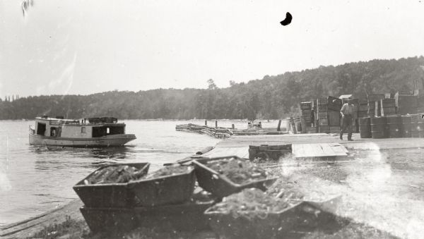 One of the four harbors on Washington Island. There is a man on a pier or dock in the foreground, and a boat approaching on the left. A tree-lined shoreline is in the distance.