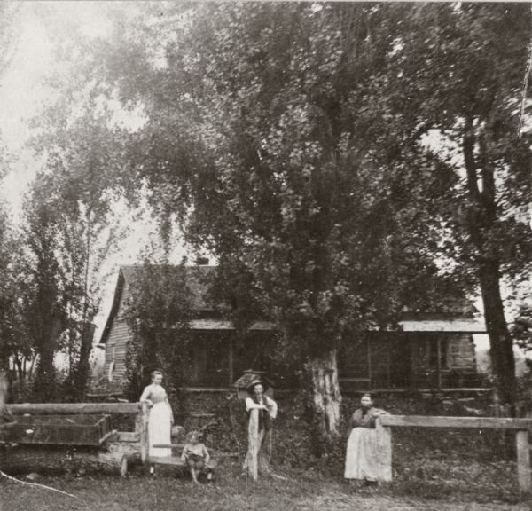 View of the Bridgeman house with three adults and a child posed along a fence in front of it.