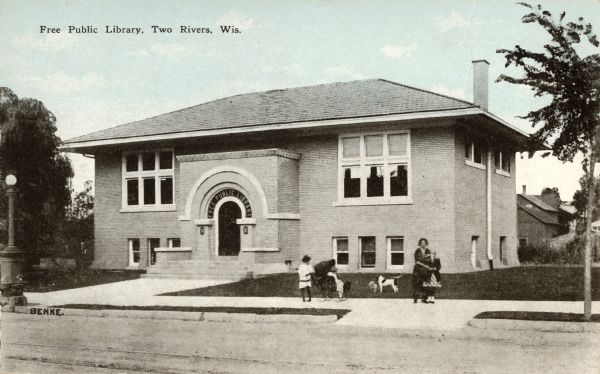 Exterior view of the Free Public Library with a woman, children, and a dog on its front lawn. Caption reads: "Free Public Library, Two Rivers, Wis."