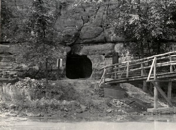 View across river towards the tunnel leading to the bottom of the shot tower shaft at Tower Hill State Park. There is a rustic bridge on the right leading to the entrance of the tunnel.