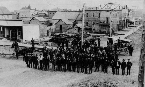 View of Superior, with a large group of men posting in a road in the foreground, and various buildings behind them.