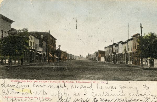 View down center of Wisconsin Avenue, with commercial buildings and storefronts on both sides. Caption reads: "Wisconsin Ave. on a Quiet Sunday Morning, Tomahawk, Wis."