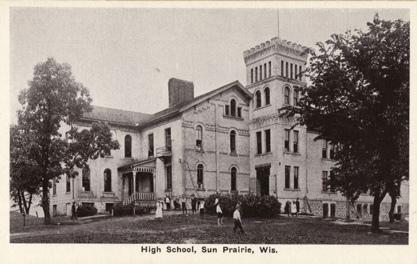 Exterior view of a high school, with multiple people standing in front of it. Caption reads: "High School, Sun Prairie, Wis."