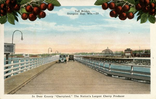 View of two automobiles crossing a toll bridge. There are cherries on branches at the top of the postcard. Caption reads: "In Door County 'Cherryland,' The Nation's Largest Cherry Producer."