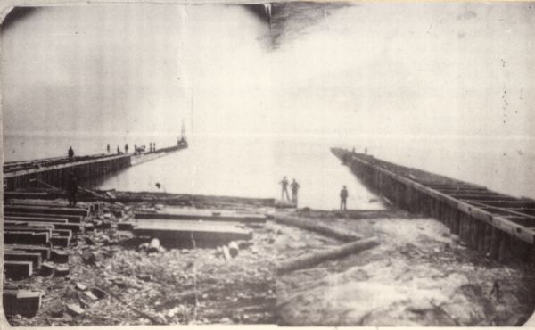 The harbor piers and the entrance to the Sturgeon Bay ship canal. Men are standing on the shoreline.