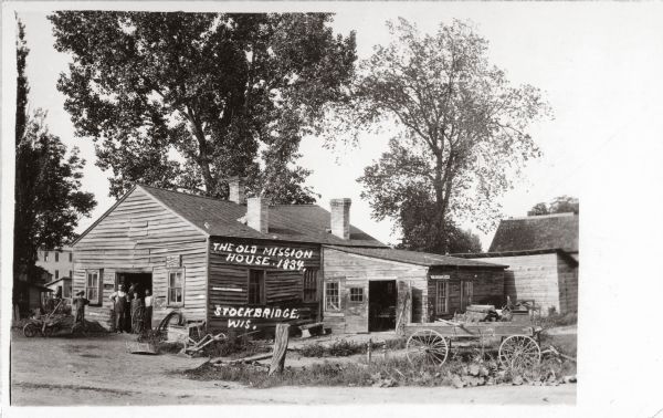 Exterior view of the Stockbridge Indian Mission, built in about 1834, with several figures and a horse standing in the structure's doorway.