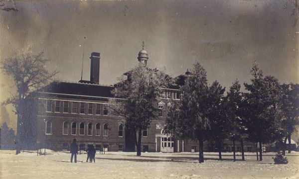 Exterior view of Wisconsin State College, otherwise known as "Normal School." People are standing in the snow in the foreground.