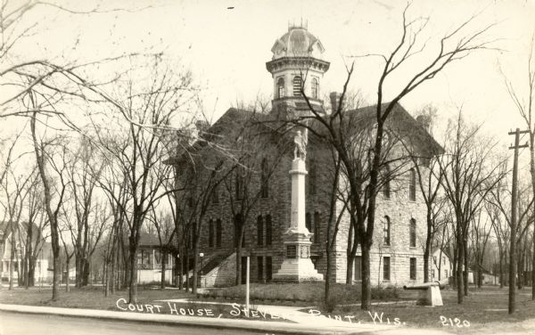 Exterior view across street towards the Portage County courthouse. A monument and a cannon are on the lawn in front. Caption reads: "Court House, Stevens Point, Wis."