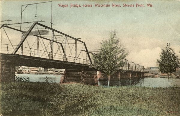 View across grass towards a wagon bridge on the left crossing the Wisconsin River at Stevens Point. Caption reads: "Wagon Bridge, across Wisconsin River, Stevens Point, Wis."