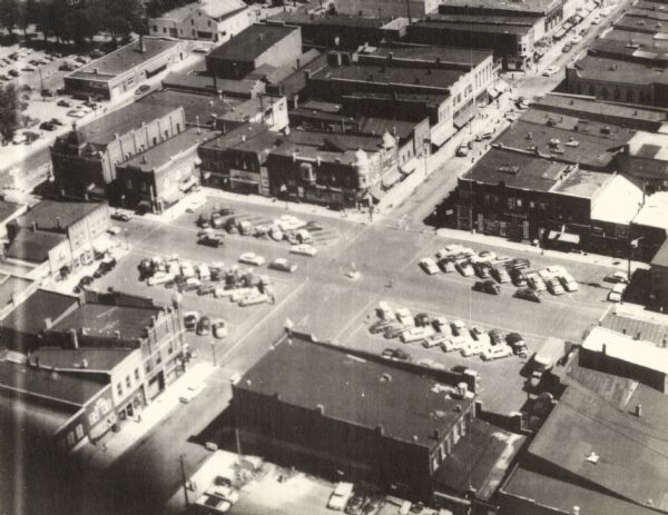 Aerial view of town, with commercial buildings, and cars in parking lots.