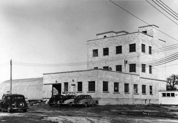 Exterior view of the Wisconsin Seed Company, Funk's Hybrid, with several automobiles parked beside it.
