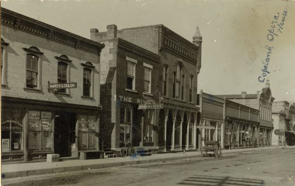 View of Water Street, looking west from the corner of Judgement Street. Businesses include a market, a tailor, and an ice cream parlor. The handwritten text reads: "Copeland Opera House."