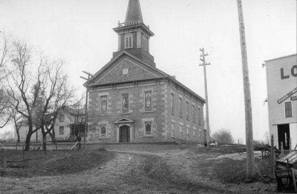 Exterior view from road towards a Methodist Episcopal church. The corner of a commercial building is on the right.
