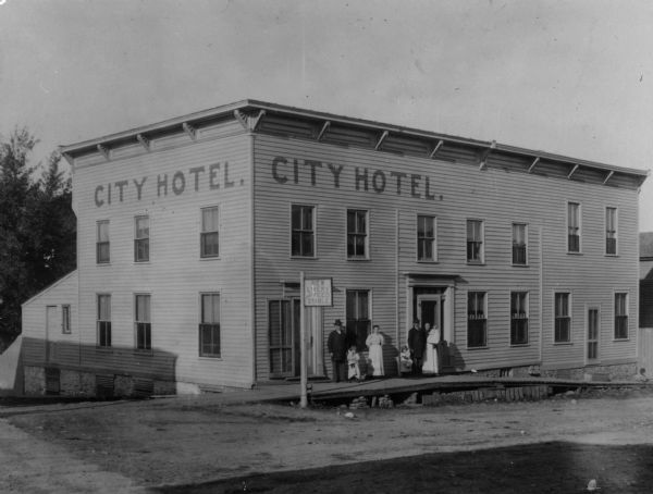 Exterior view of the City Hotel with a group of people posed near its entrance.