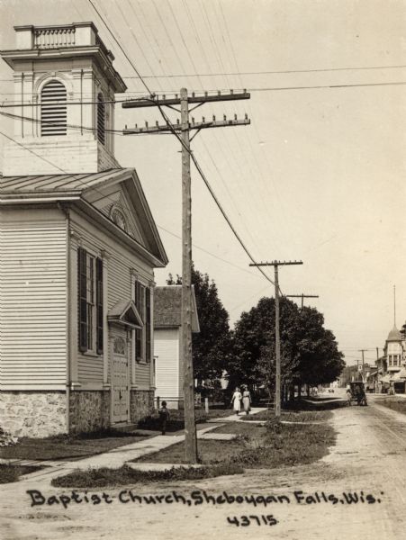 View down road and sidewalk towards a Baptist church. Caption reads: "Baptist Church, Sheboygan Falls, Wis."