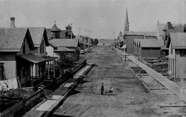 Elevated view of South Twelfth Street. There is a child standing in the center of the street holding onto a wagon in which another child is sitting. A church is in the background on the right.