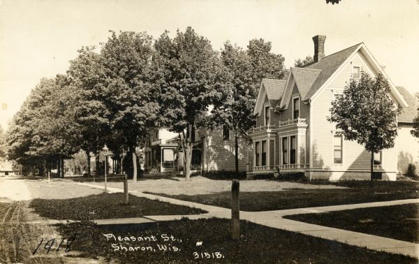 View from road towards the right side of the tree-lined street with a sidewalk and houses. Caption reads: "Pleasant St., Sharon Wis."