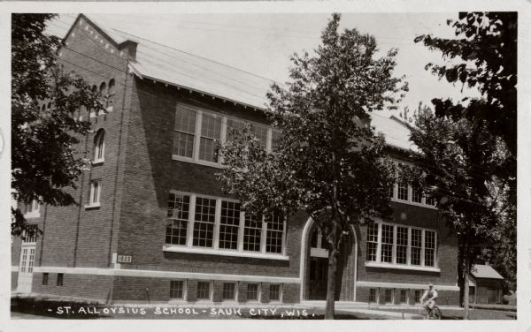 Exterior view of St. Aloysius School with a figure on a bicycle riding past it in the foreground.