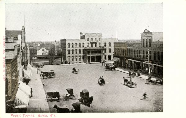 Elevated view of a public square filled with horse-drawn carriages and pedestrians. Caption reads: "Public Square, Ripon, Wis."
