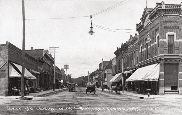 View of Court Street looking west. Caption reads: "'Court St. Looking West' Richland Center, Wis." The awning over the storefront on the right corner reads: "Clothing. Edwards & Kelly. Shoes." A storefront further down the street on the left has a sign that reads: "The Boston Store".