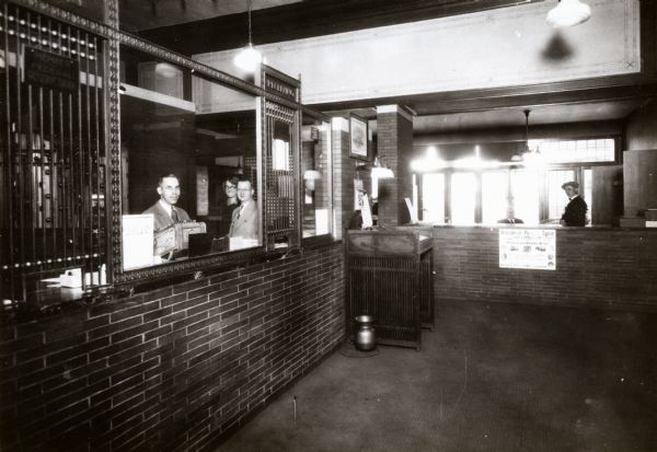 View showing the original interior of the First National Bank, with several individuals standing behind the teller stations.