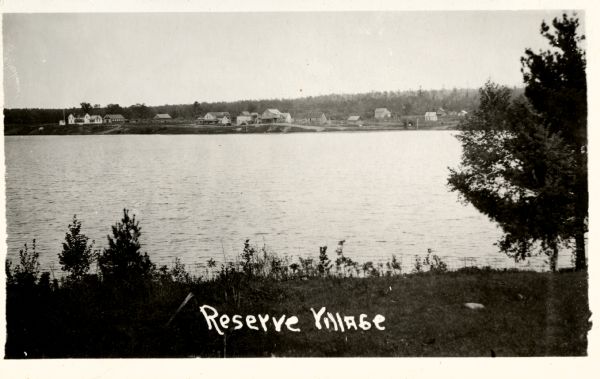 View from shoreline towards a village across a body of water. Caption reads: "Reserve Village".