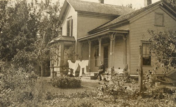 Exterior view of the Kipp residence with laundry hanging in front and a man seated on the porch.