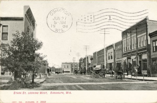 Caption reads: "Stark St. Looking West, Randolph, Wis." Horse-drawn vehicles are parked along the curb on the right.