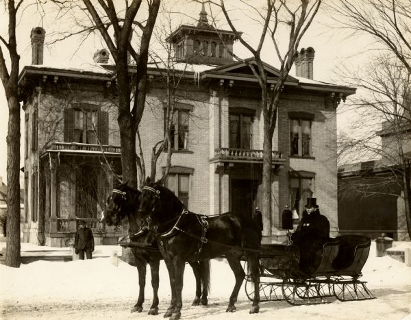 Winter scene at the Case Residence with J. I. Case's sleigh and team.  Andrew Jackson, hostler, (died Dec., 1924) is in the sleigh and "Nick" Mitchell, hired man, is standing near the house at the left.
