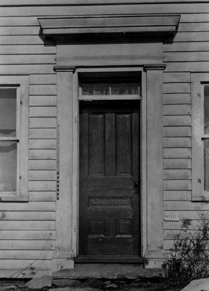 Front entrance detail of the Vanderpool farmhouse. A ruler is mounted on the left door frame, and a sign on the right at the base of the doorframe reads: "WIS-115".