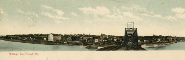 Panoramic view of Prescott, including multiple buildings, and a view down the center of a railroad bridge. Caption reads: "Greetings from Prescott, Wis."