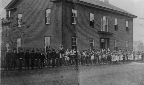 Exterior view of a school building with a group of children and adults gathered in front.