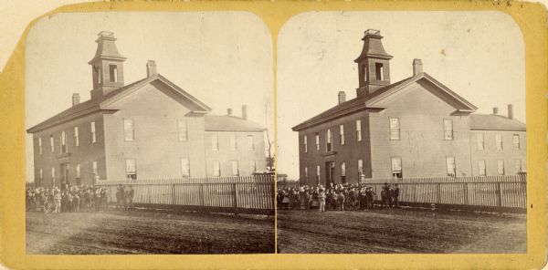 Stereograph view across road towards a school building with children gathered outside.