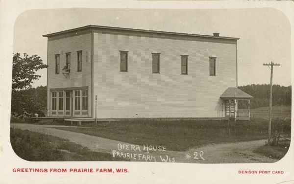 View across road towards the front and right side of the Opera House. Caption reads: "Greetings from Prairie Farm, Wis."