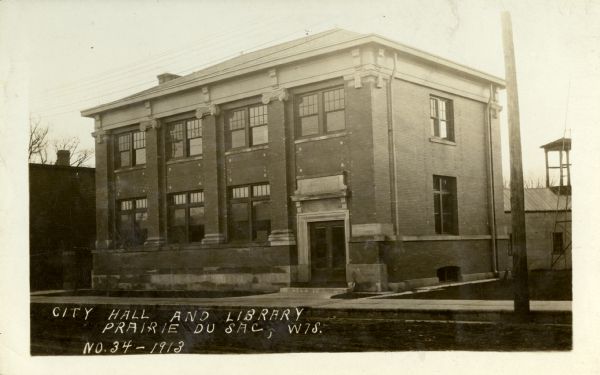 View from street towards the building. Caption reads: "City Hall and Library, Prairie du Sac, Wis."