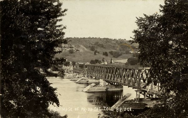 Elevated view from shoreline of toll bridge across the Wisconsin River. Caption reads: "A Glimpse of Pr-Du-Sac Toll Bridge."