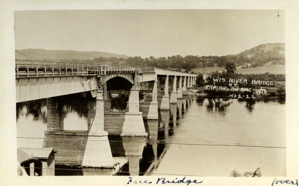 View along side of bridge over the Wisconsin River, built in 1921 to take the place of the old wooden one when it became condemned. Caption reads: "Wis. River Bridge, Prairie du Sac, Wis."