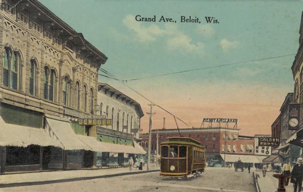 Trolley car driving along Grand Avenue, with people walking on the sidewalks next to storefronts. Caption reads: "Grand Ave., Beloit, Wis."